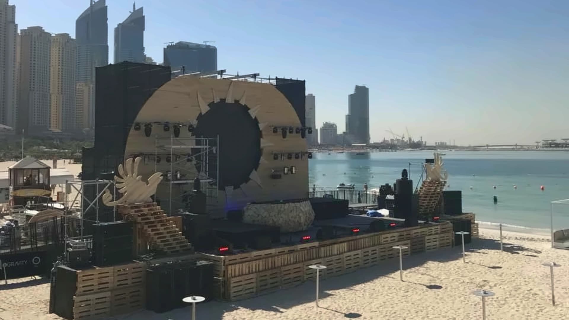 Beachfront concert stage with temporary scaffolding, lighting and a waterfront skyline