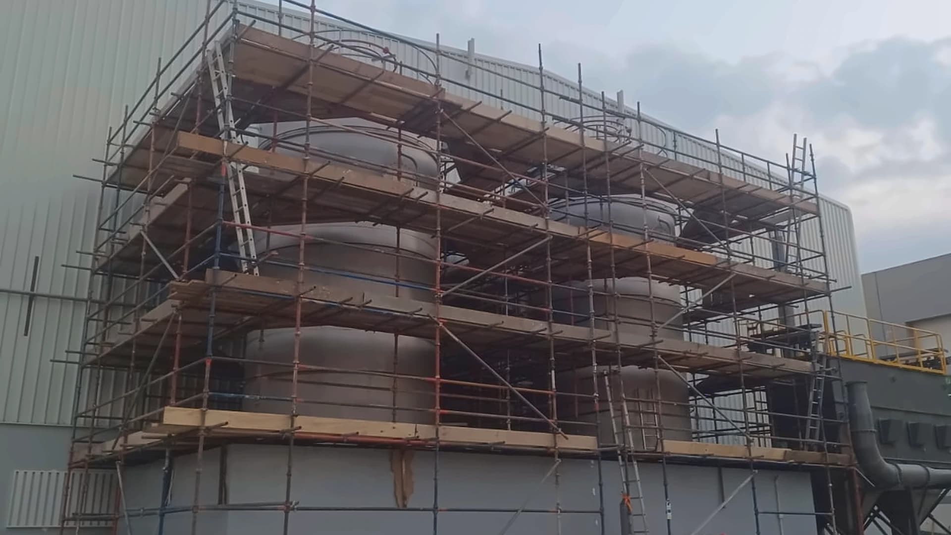 Multi-level scaffolding around industrial tanks and pipework at a facility