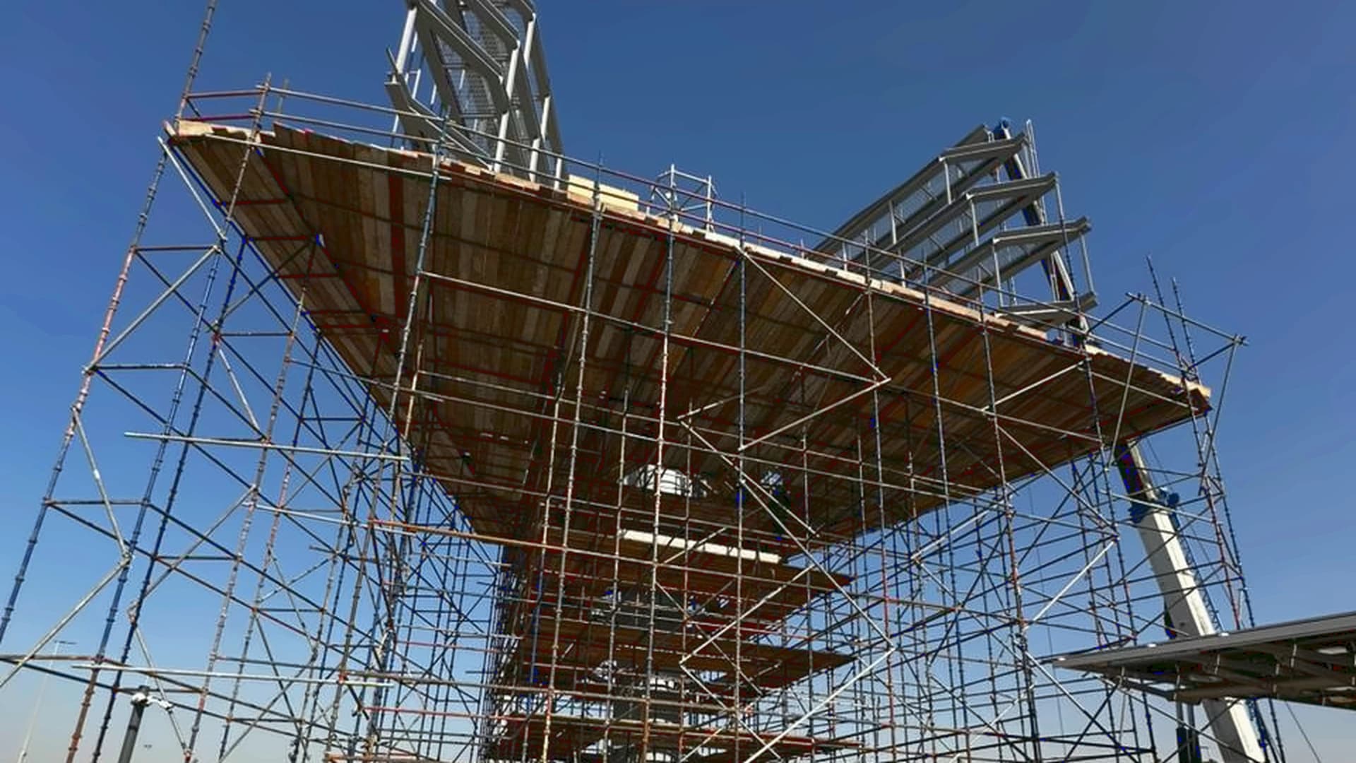 Elevated scaffold platform around a steel structure under construction beneath a blue sky